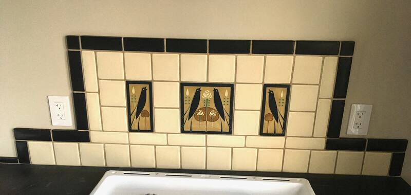 Cream tile backsplash with black trim and three bird art tiles above a sink