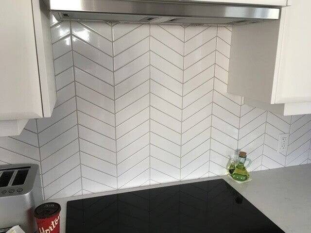 White chevron tile kitchen backsplash with grey grout under a stainless steel range hood