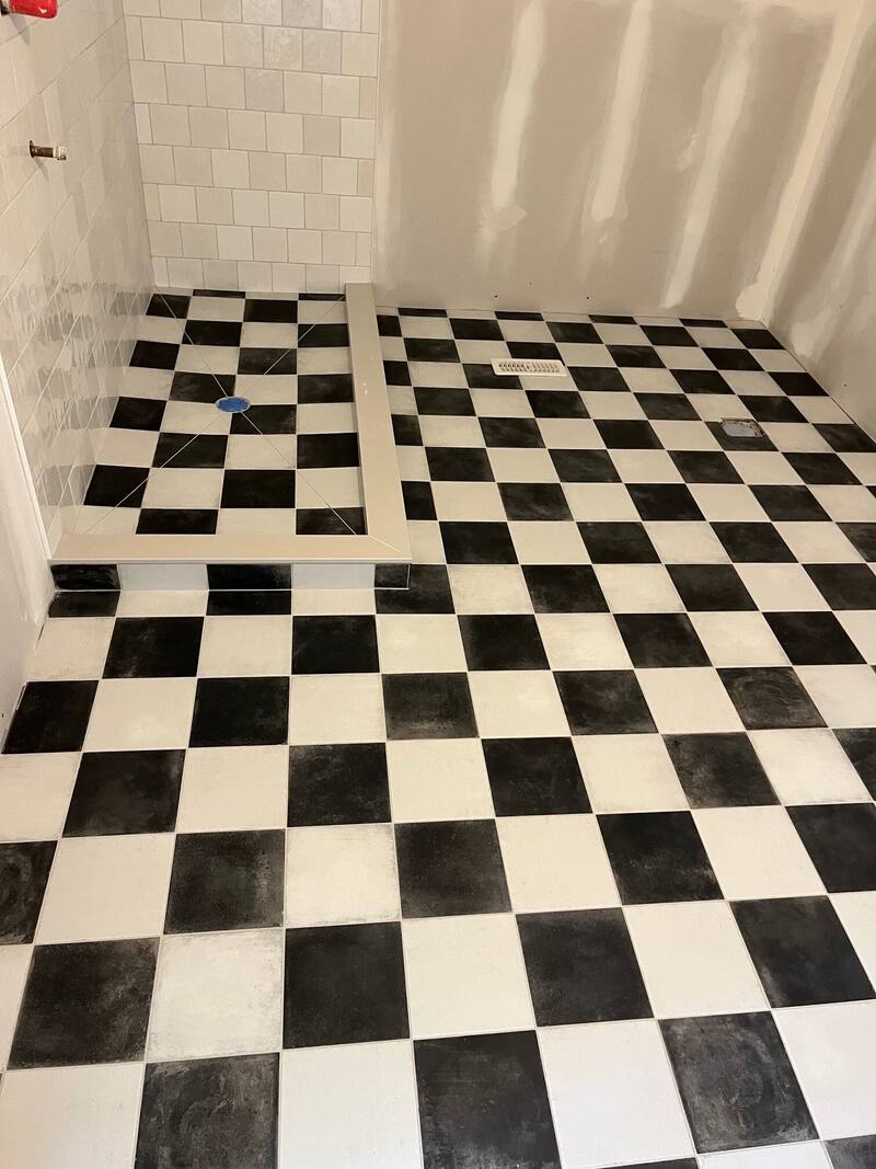 Black and white checkerboard floor tile running into a tiled shower curb