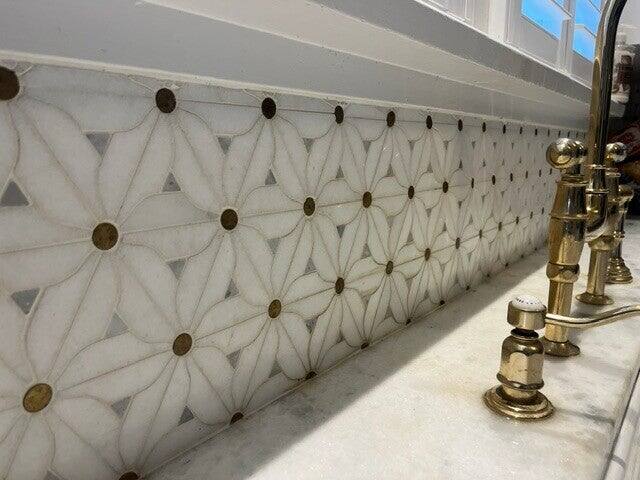 Marble flower pattern backsplash with brass dot inserts behind a brass faucet