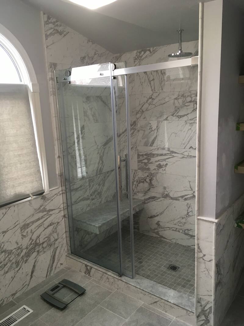 Shower with marble-look wall tile, a bench, a mosaic floor and a sliding glass door