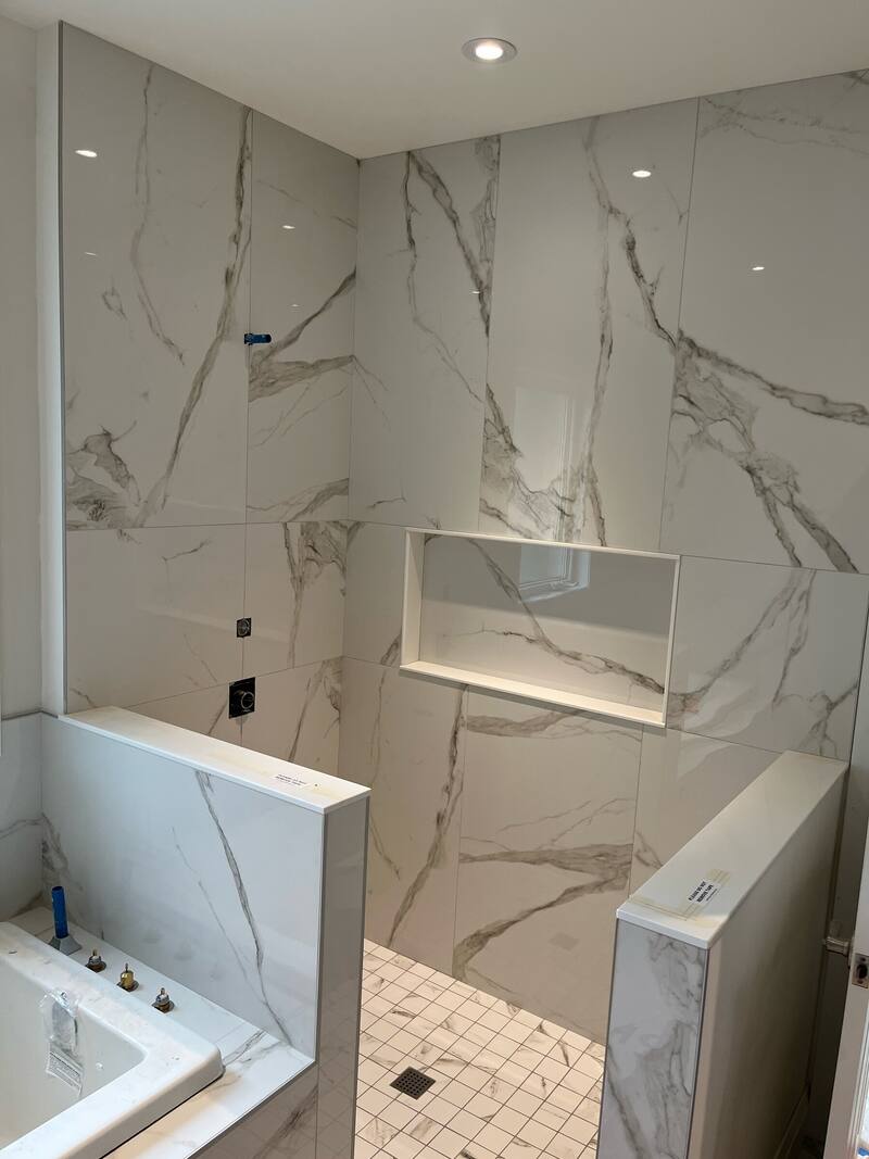 Walk-in shower with large-format marble-look wall tile, a recessed niche and a tub beside it